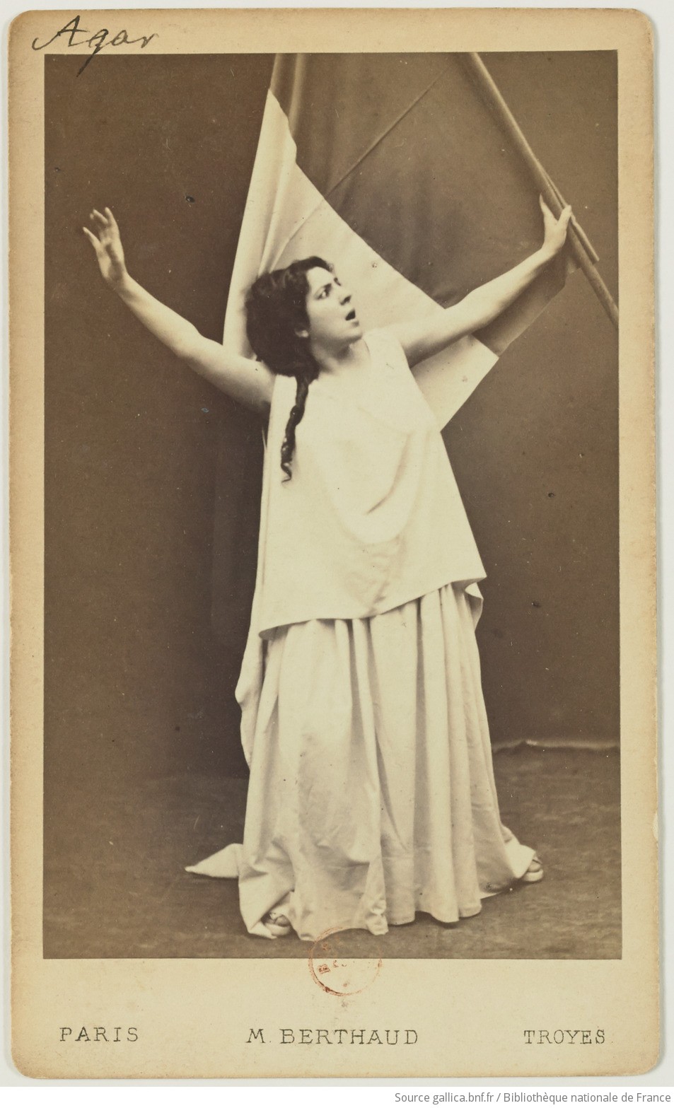 Image of a woman wearing white standing in front of a French flag.