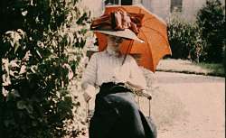 Jeune femme à ombrelle rouge assise dans un jardin. 1907-1920