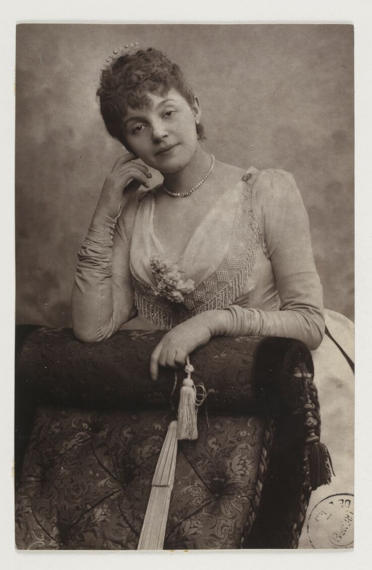 Photo en noir et blanc de l'actrice Réjane, amie de Marie Arconati-Visconti, posant en robe élégante, appuyée sur un fauteuil orné.